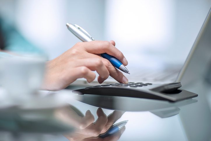 Martinson & Carter, CPAs, PA | close up of a hand holding a pen and working on a calculator near a laptop in the background